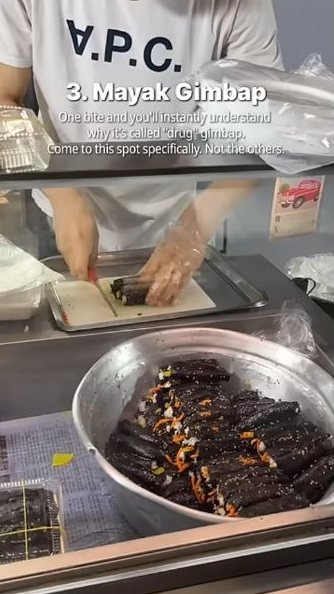 Small gimbap rolls in a metal bowl while a vendor prepares more behind the counter.