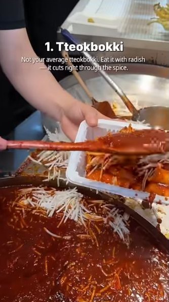 Sauce being spooned over rice cakes and shredded radish in Bae’s Gwangjang Market short.