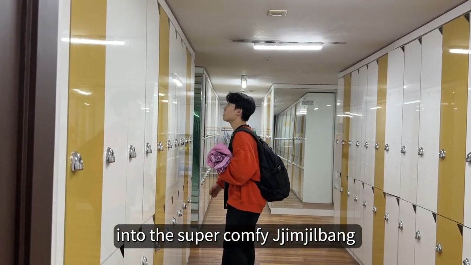 Bae holding folded spa clothes beside tall clothes lockers
