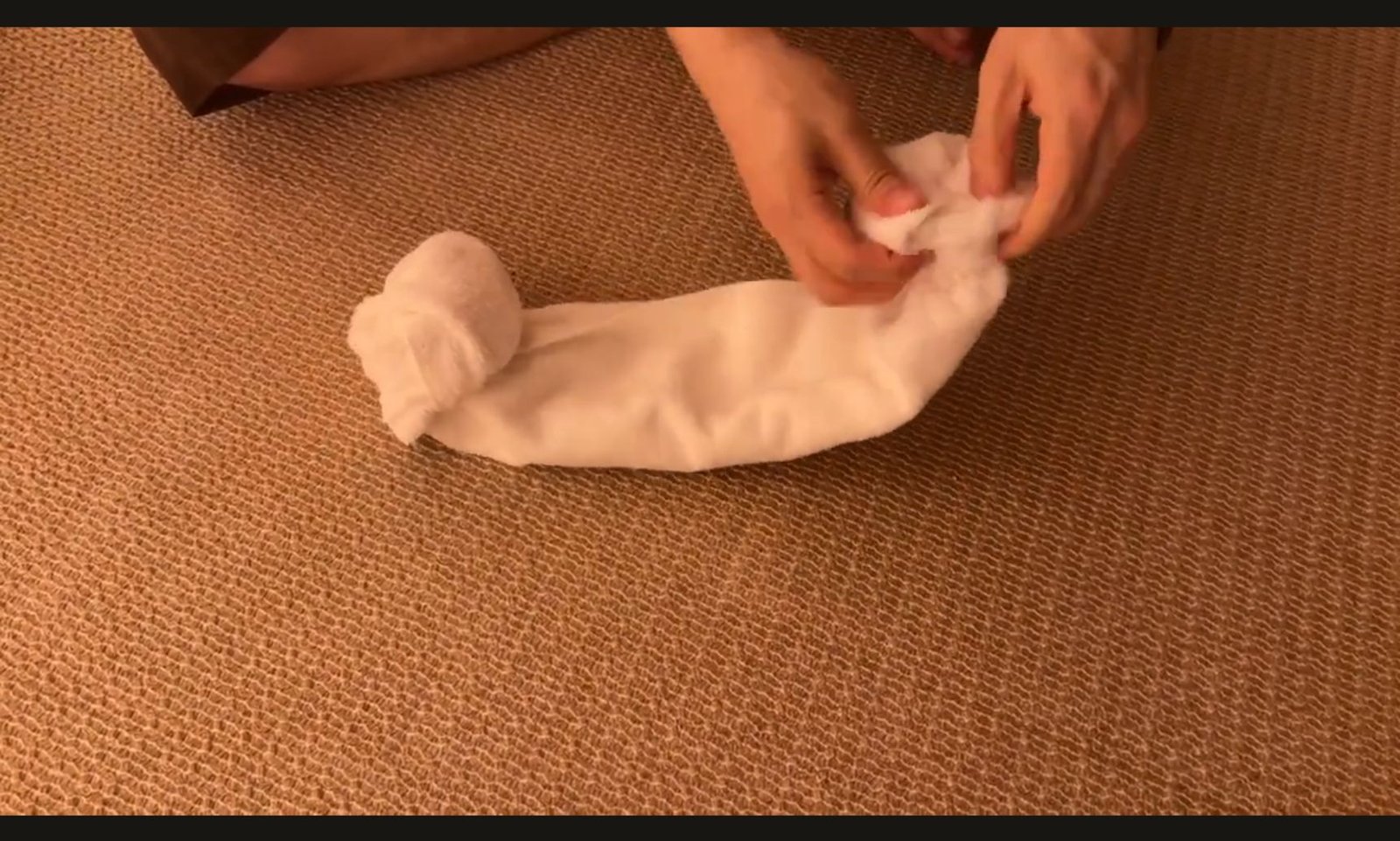 Hands rolling both ends of a folded towel into a sheep-head towel hat